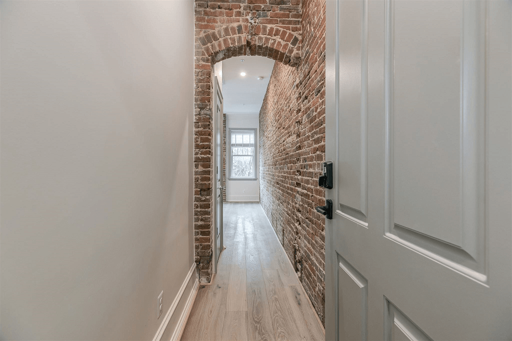 a hallway with an exposed brick wall and a white door